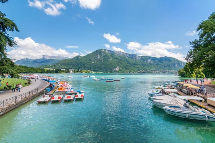 Explore the picturesque Lake Annecy with boats and mountains under a clear sky.
